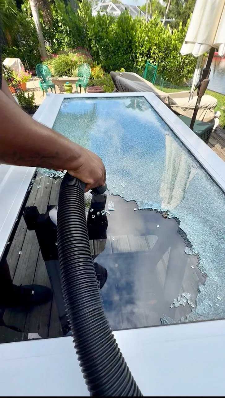 SliderPro technician vacuuming shattered tempered glass off a sliding door panel beside a pool
