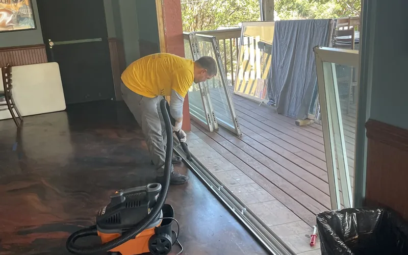 SliderPro technician vacuuming debris out of a sliding door track with the panel lifted out