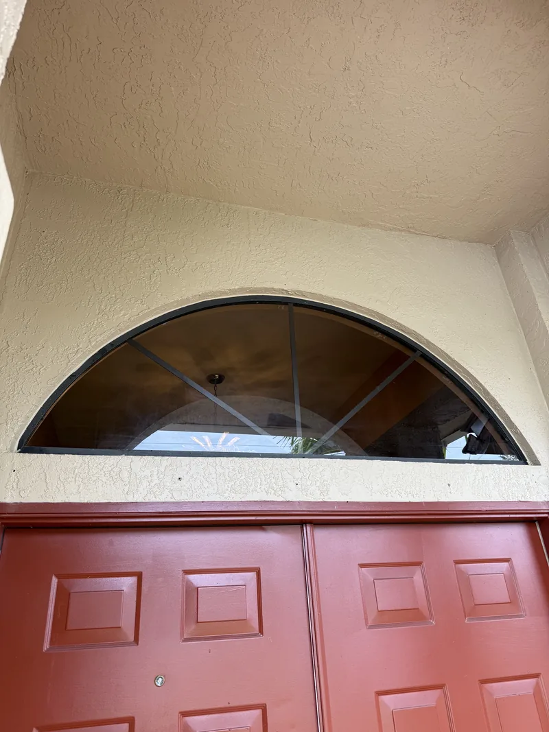 Half-round entry transom with new bronze glass and radial muntin bars, fitted into the original stucco opening