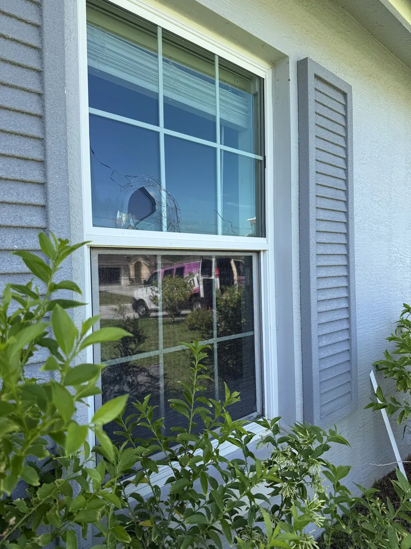 Impact window pane with a clean strike point and cracks radiating outward, the glass still fully held in the sash by its laminated interlayer